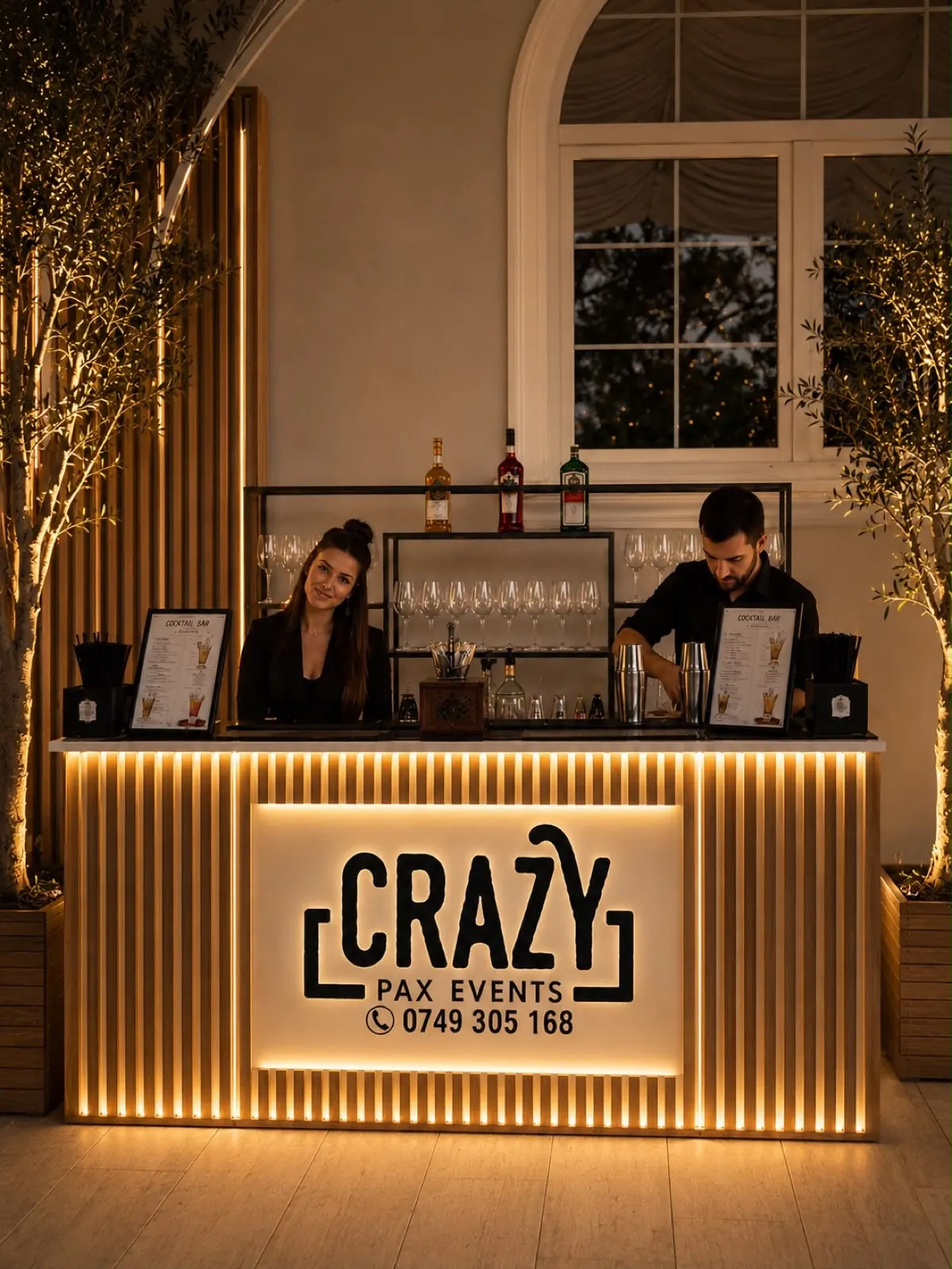 Doi barmani Crazy Pax la barul cu lumini aurii, într-o sală de nuntă